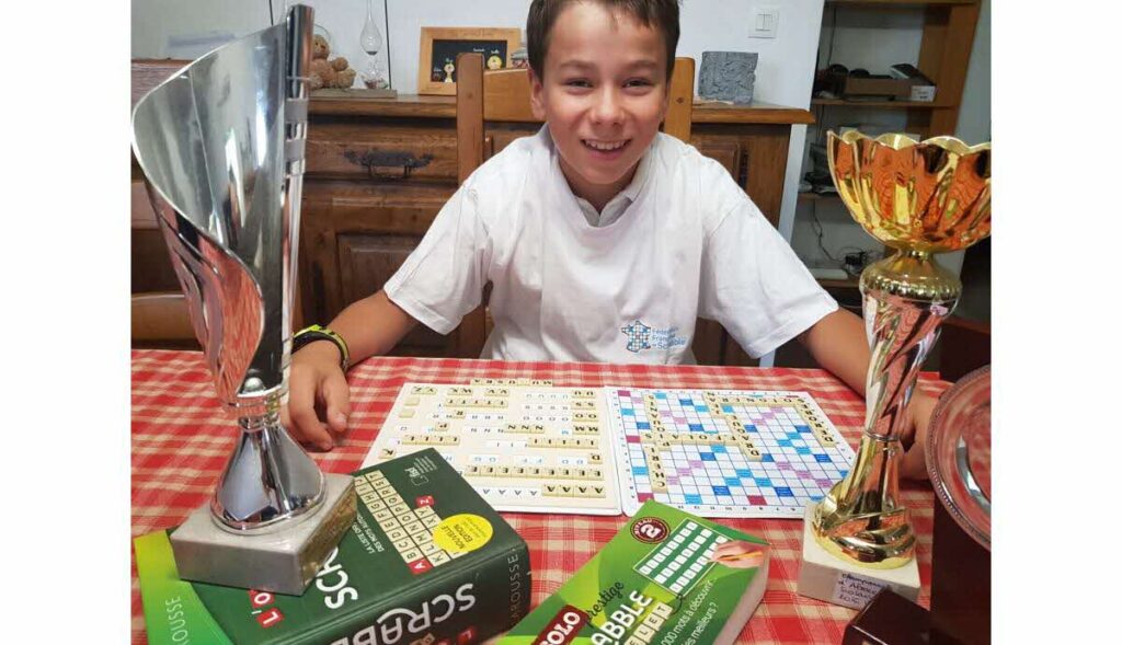 Jeune joueur de Scrabble utilisant un mot de 8 lettres, illustrant le plaisir du jeu de lettres